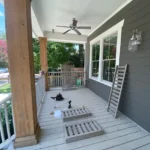 A porch with a black cat laying on the ground.