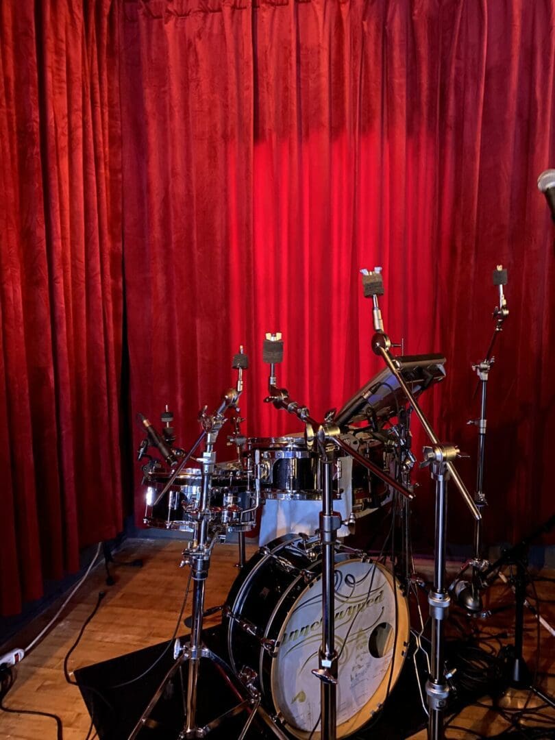 A drum set in front of red curtains.