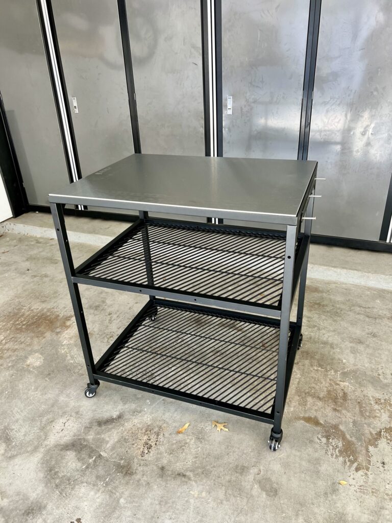 Black metal workbench assembly services in Houston with a stainless steel top and wire shelves.