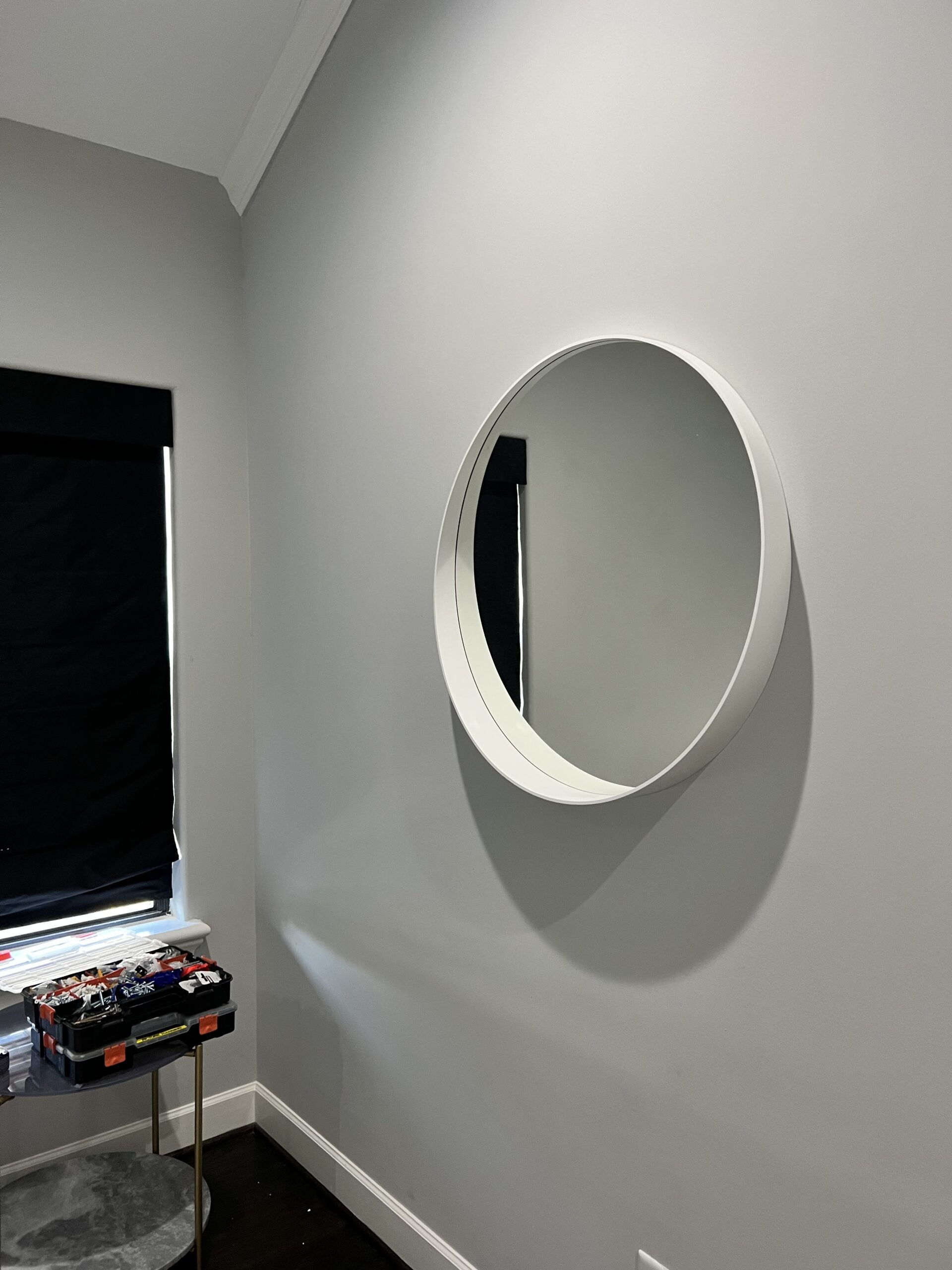 Minimalist bedroom featuring a round mirror on a grey wall, reflecting a sleek, modern design.