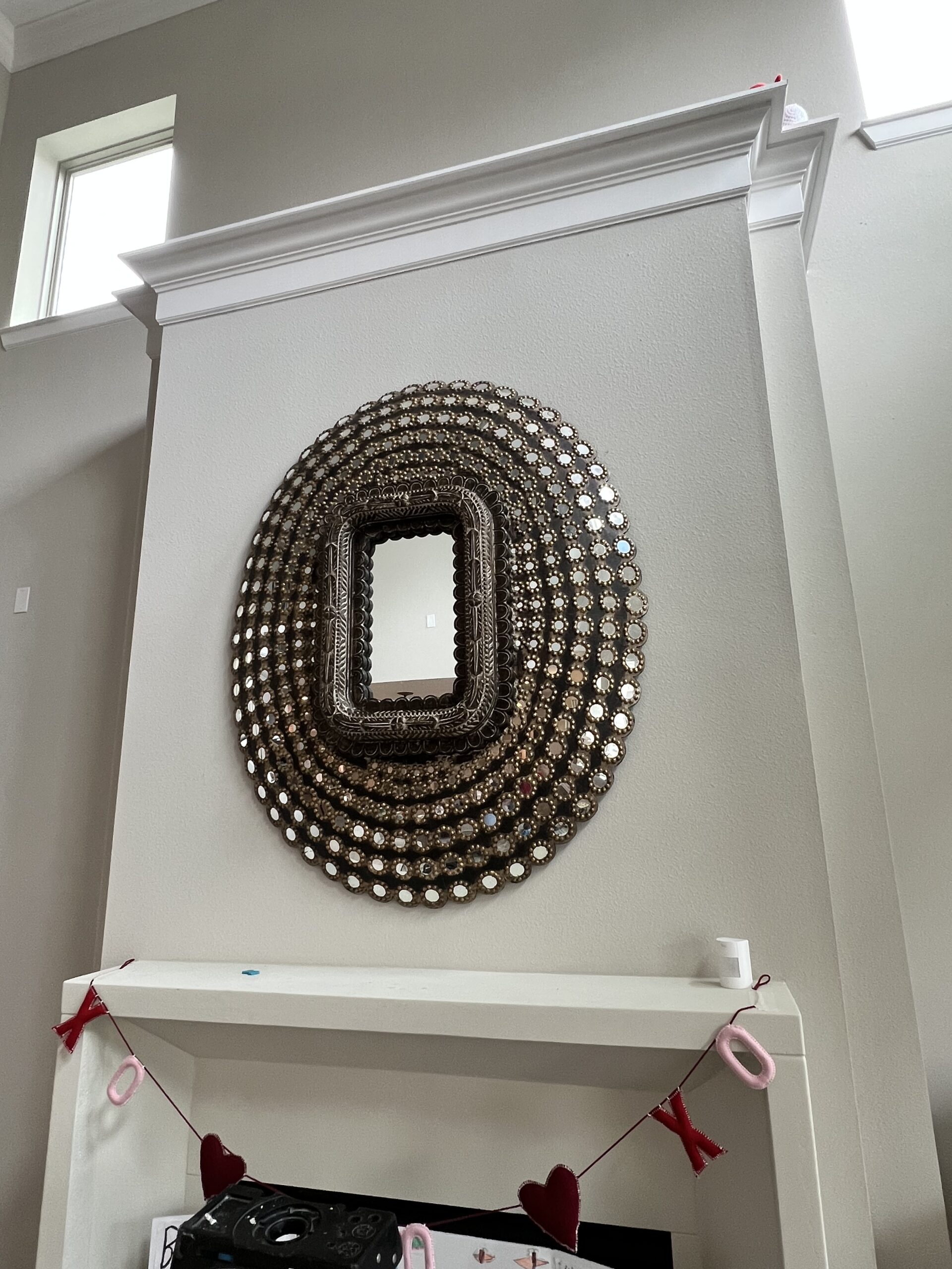 Ornate round mirror mounted above a fireplace, showcasing decorative mirror installation services.