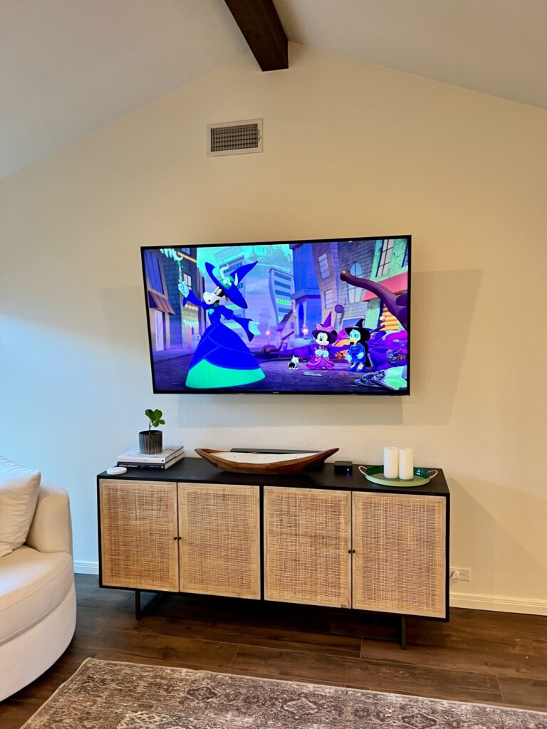 A curved TV mounted on the wall above a rattan console table in a modern living room.