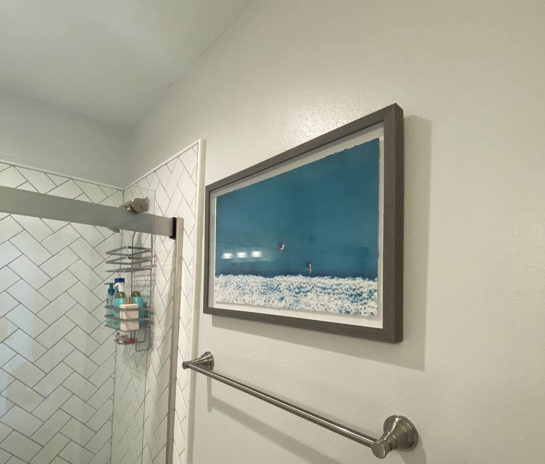 Framed ocean scene mounted in a bathroom, showcasing professional picture mounting.